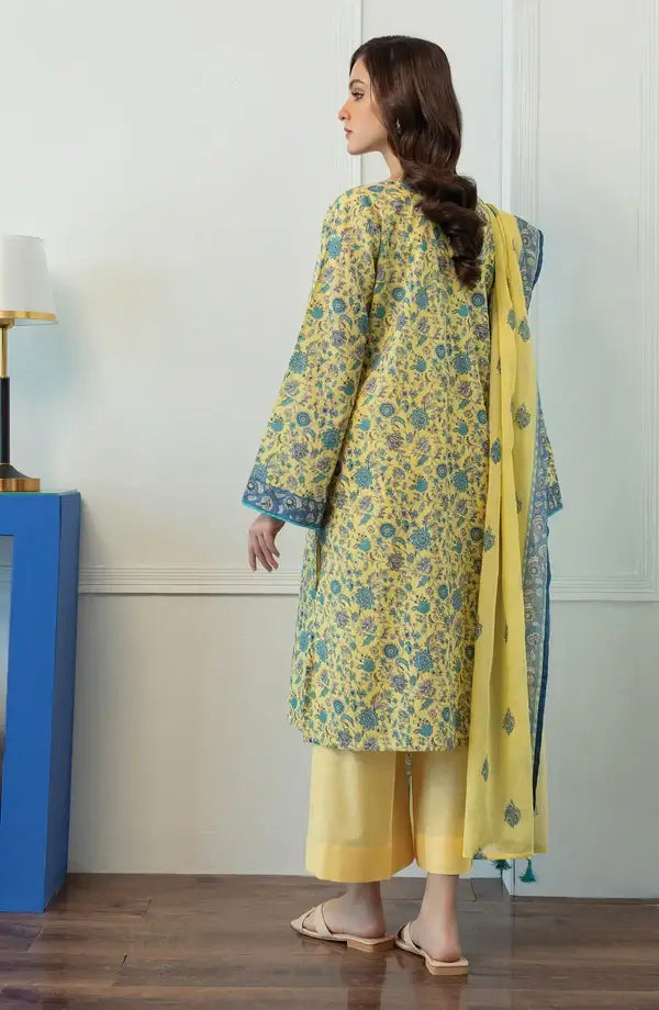 A woman wearing a yellow and teal floral printed traditional kurta set with matching pants and dupatta, shown from the back in an indoor setting.