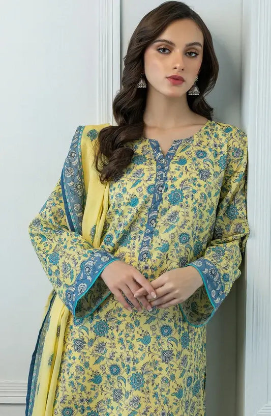 A woman modeling a yellow and blue floral printed kurta with a matching dupatta, standing against a white paneled wall.
