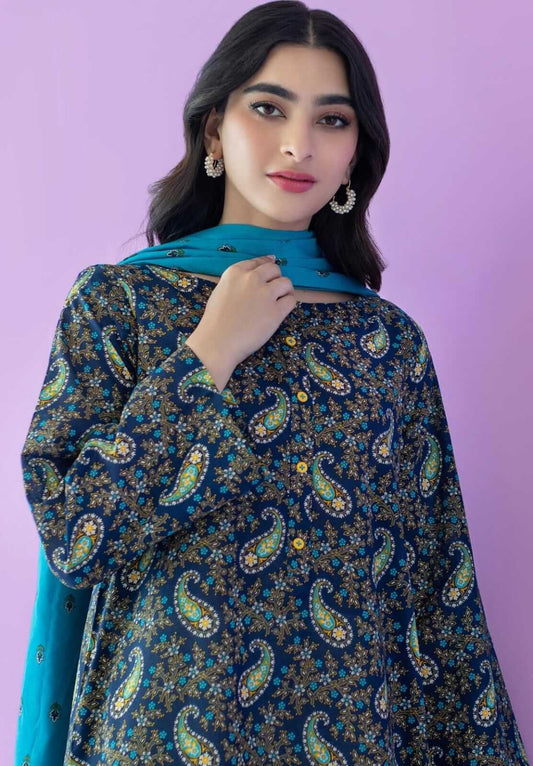 A woman modeling a dark navy blue printed kurta with intricate paisley and floral motifs in green, gold, and white, paired with a bright turquoise dupatta, set against a solid lavender background.