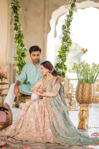 Hania Embroidered Net Gharara worn by a couple in a beautifully decorated outdoor setting with floral arrangements.