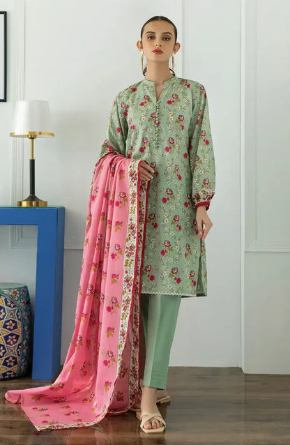 A woman models a three-piece Indian ethnic salwar kameez suit set. The set includes a sage green long-sleeve kurta with pink and red floral prints, matching sage green trousers, and a vibrant pink dupatta with a gold border and floral print.