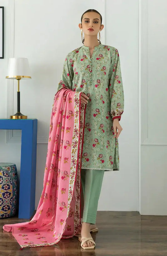 A woman models a three-piece Indian ethnic salwar kameez suit set. The set includes a sage green long-sleeve kurta with pink and red floral prints, matching sage green trousers, and a vibrant pink dupatta with a gold border and floral print.