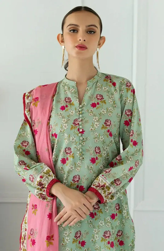 A woman modeling a mint green floral printed kurta with a pink dupatta featuring a matching floral pattern, set against a clean white paneled wall.
