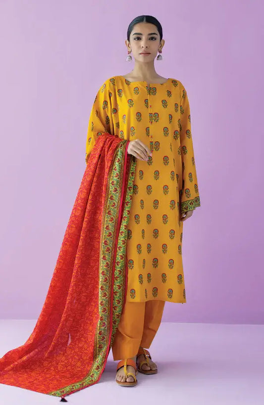 A woman modeling a mustard yellow kurta with small green motifs, paired with matching yellow trousers and a red dupatta featuring a green border, set against a solid lavender background.
