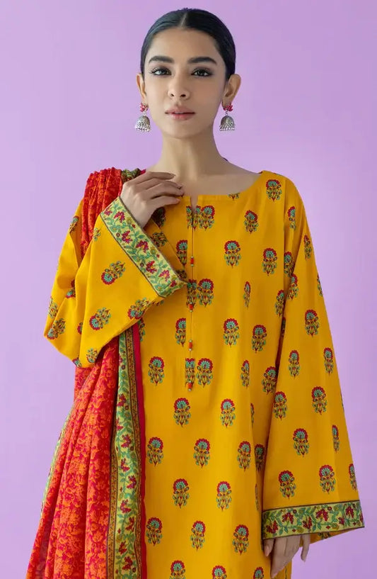 A woman modeling a yellow kurta with small multicolor floral prints and a red dupatta with green borders, set against a solid lavender background.
