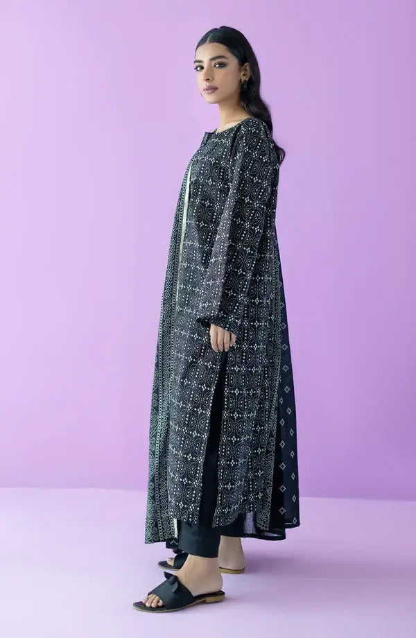 A woman modeling a long black kurta with white geometric patterns, paired with black pants and black slide sandals, set against a solid lavender studio backdrop.