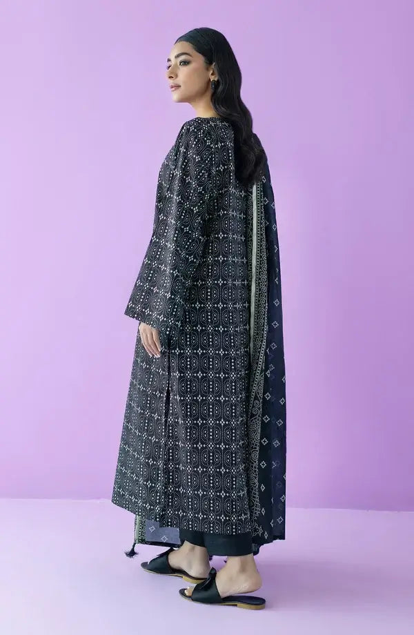A woman modeling a long black kurta with white geometric patterns and a matching printed dupatta, standing against a solid lavender-purple studio background.