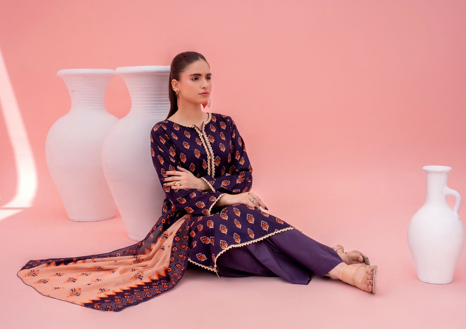 Woman in a traditional outfit sitting on a pink floor with white vases.